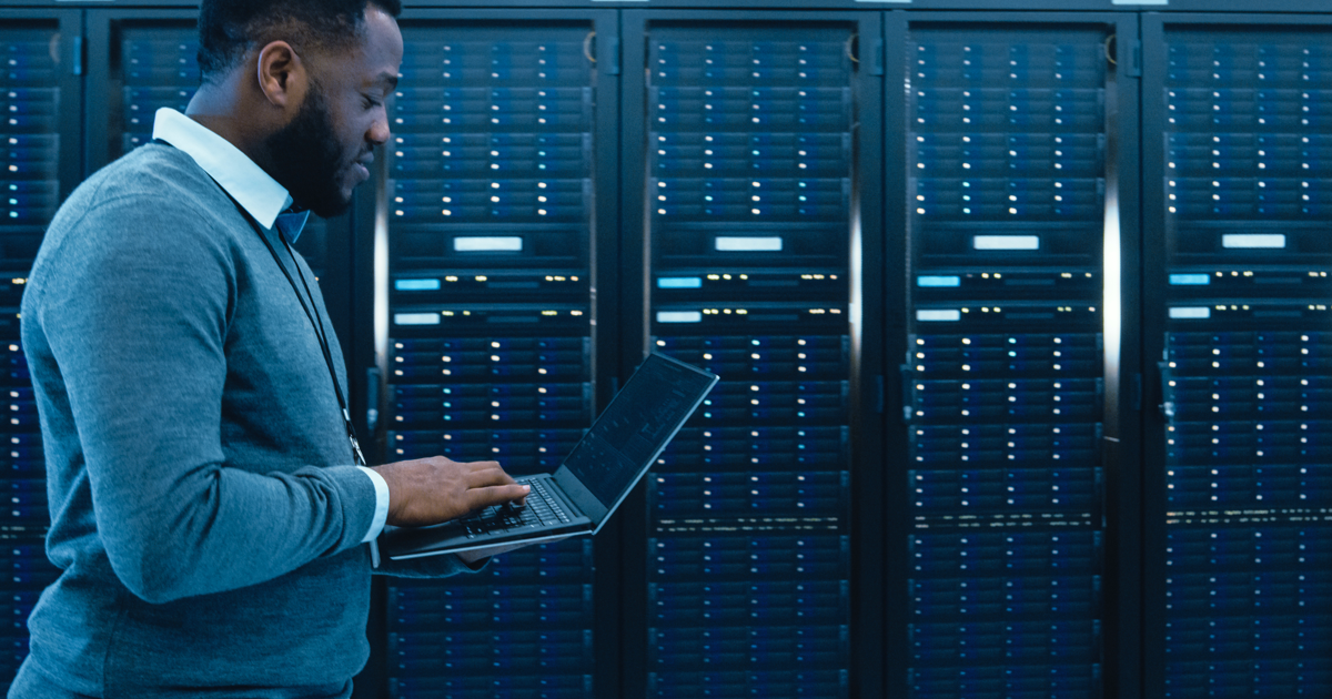 Young African-American man looking at laptop in server room